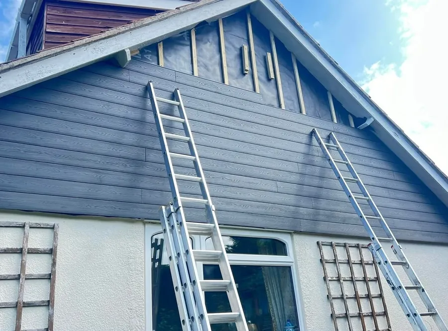 Composite cladding boards being fitted to a gable end from ladders