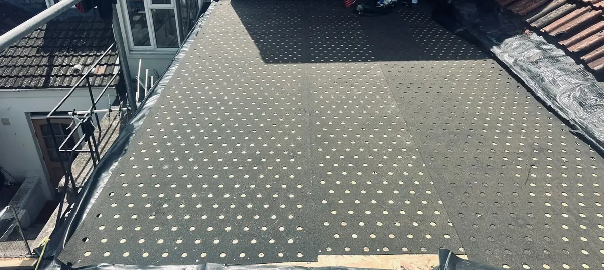 Perforated venting underlay laid across a flat roof deck before felting